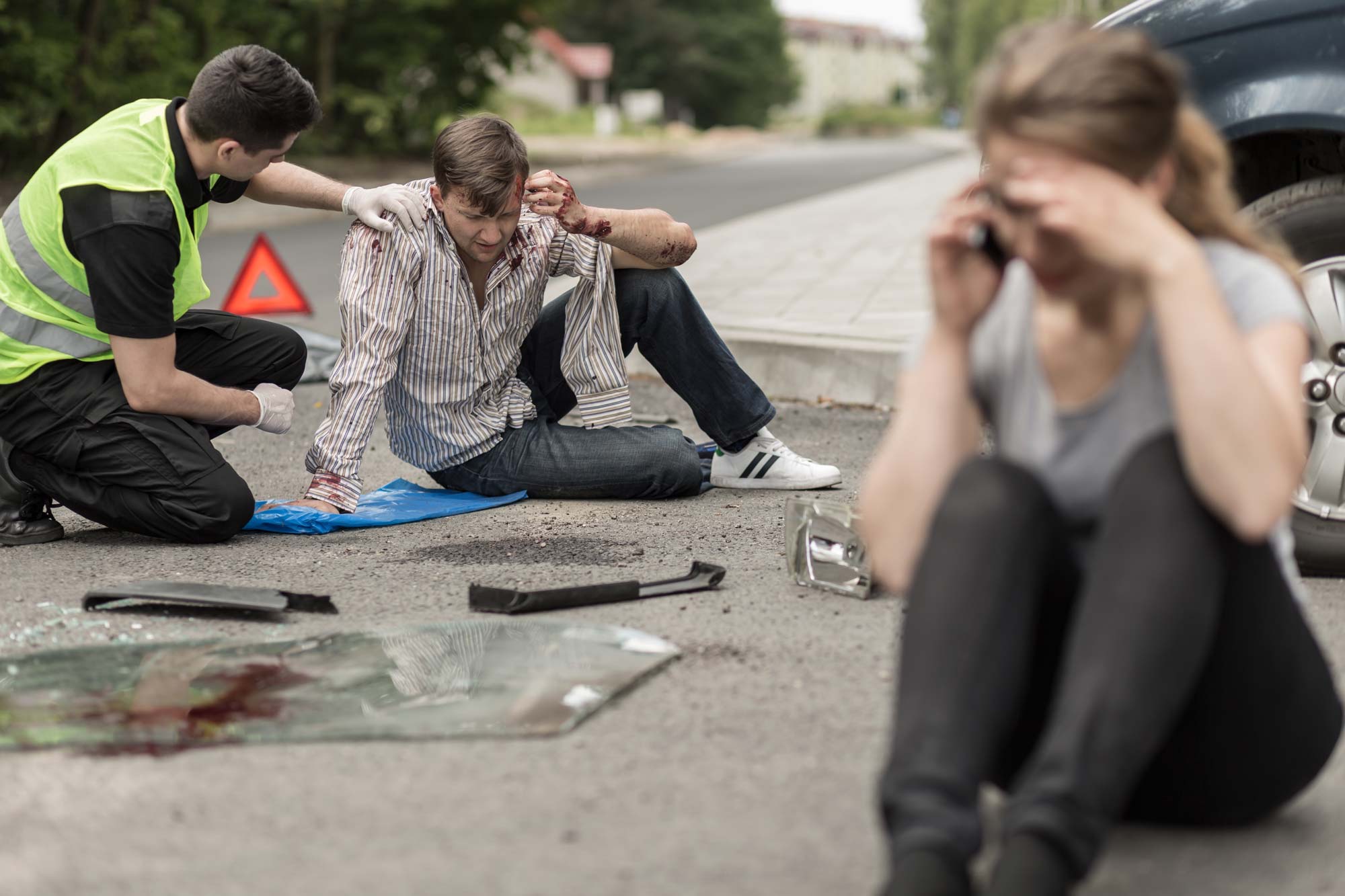 man providing first aid after car accident and woman on phone